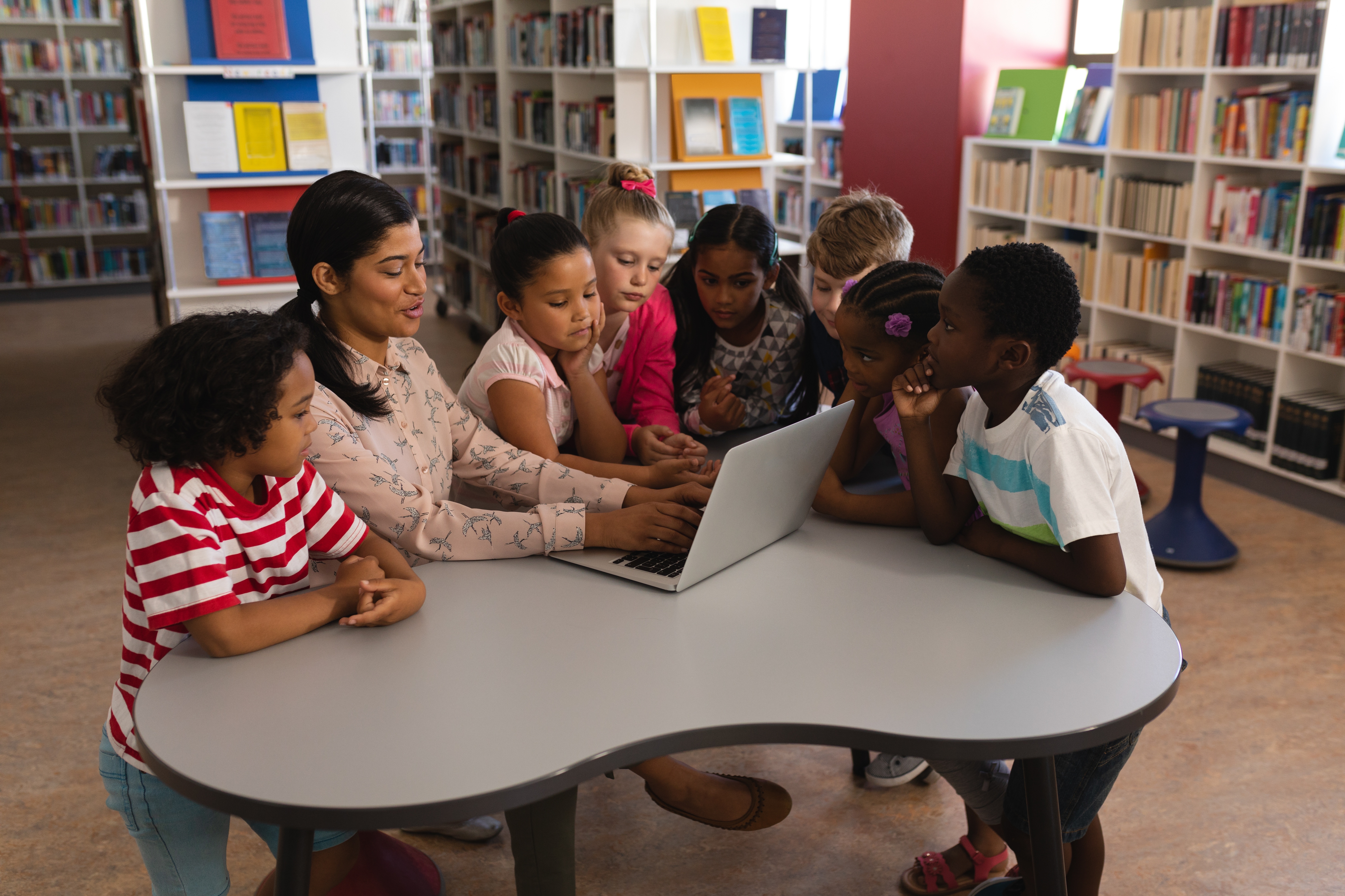 Kids and teacher in a library connected to other libraries through network engineer technology.